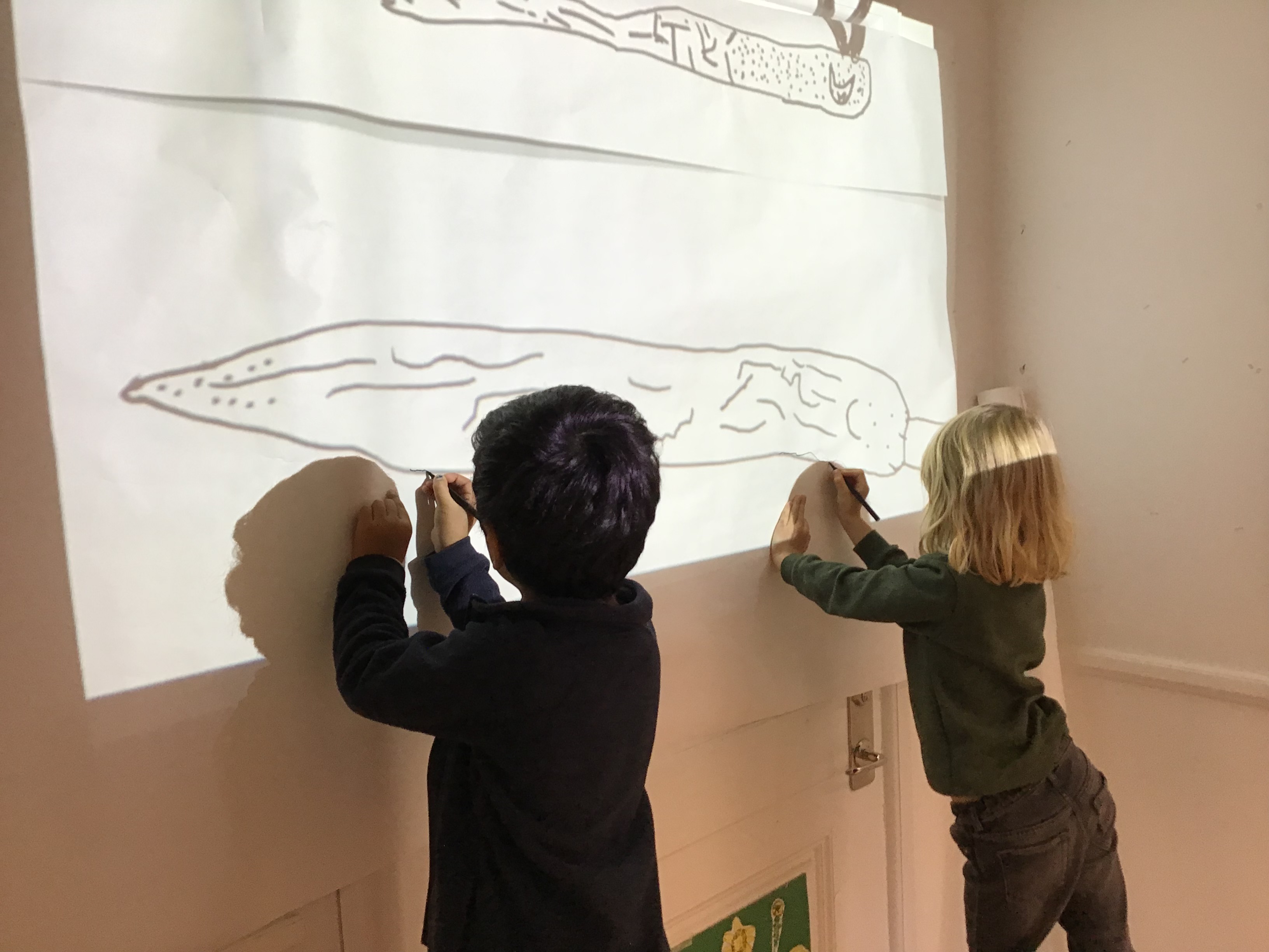 Två barn målar av en bild som projiceras på väggen
