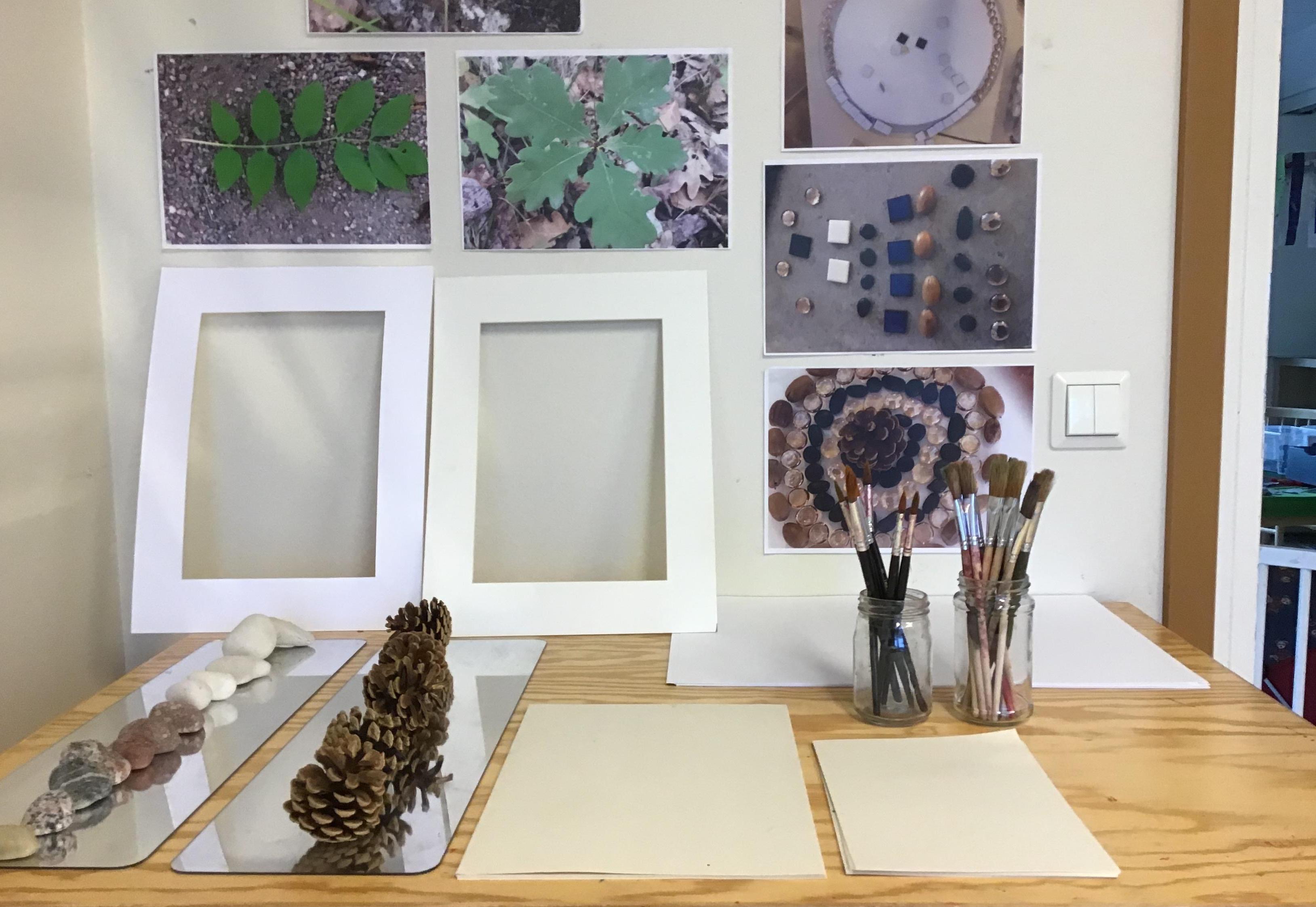 Bild på ett skrivbord i ateljén med penslar, papper och naturmaterial.
