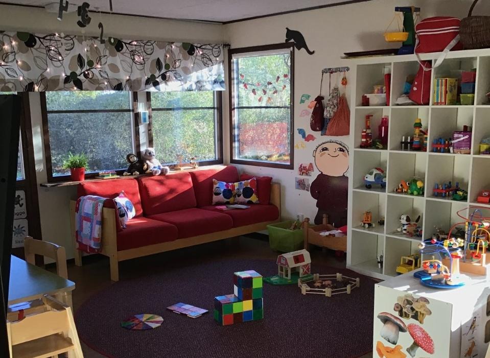 En bild på ett rum för olika lekar och aktiviteter. Till höger finns olika leksaker i en hylla. Rakt fram finns en soffa och på golvet en större matta. 